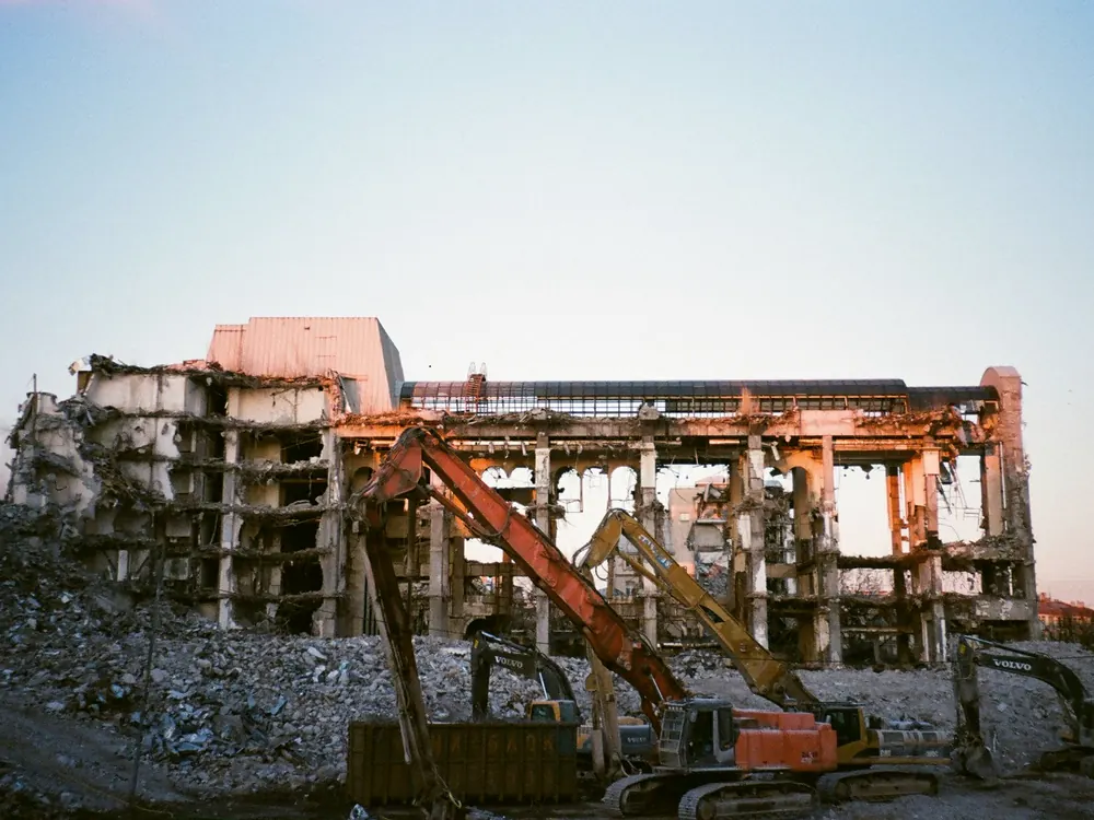 Excavator tearing down an old structure at sunset